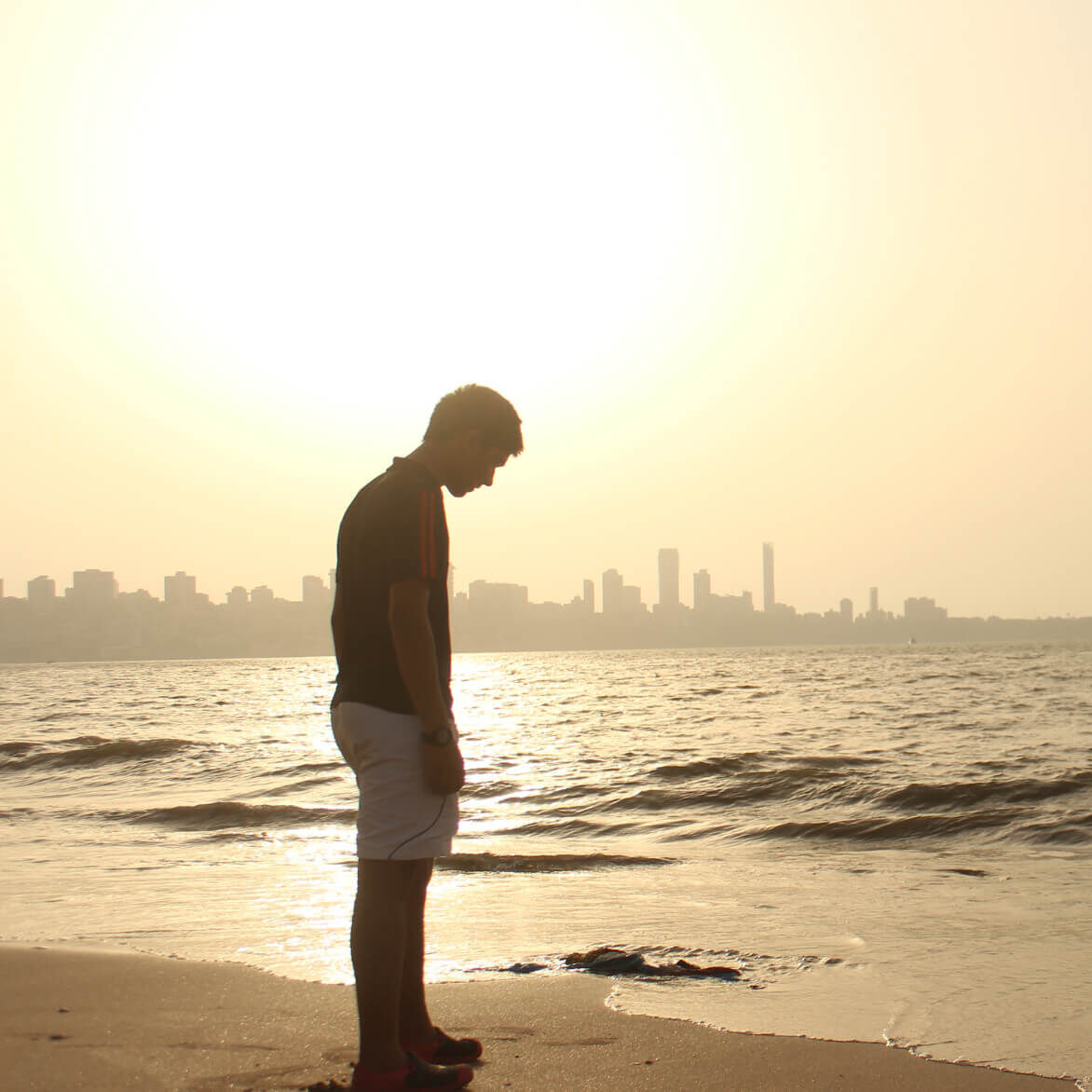 a despondent man stands on the shore looking down